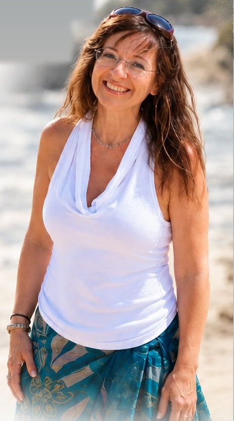 Mel smiling on a beach in a white top and teal wrap skirt